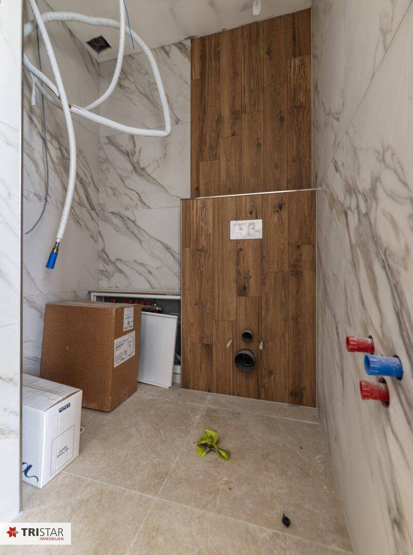 Badezimmer im Bau mit Marmoroptik-Fliesen, Holzpaneelen und vorbereiteten Anschlüssen für Sanitäranlagen.