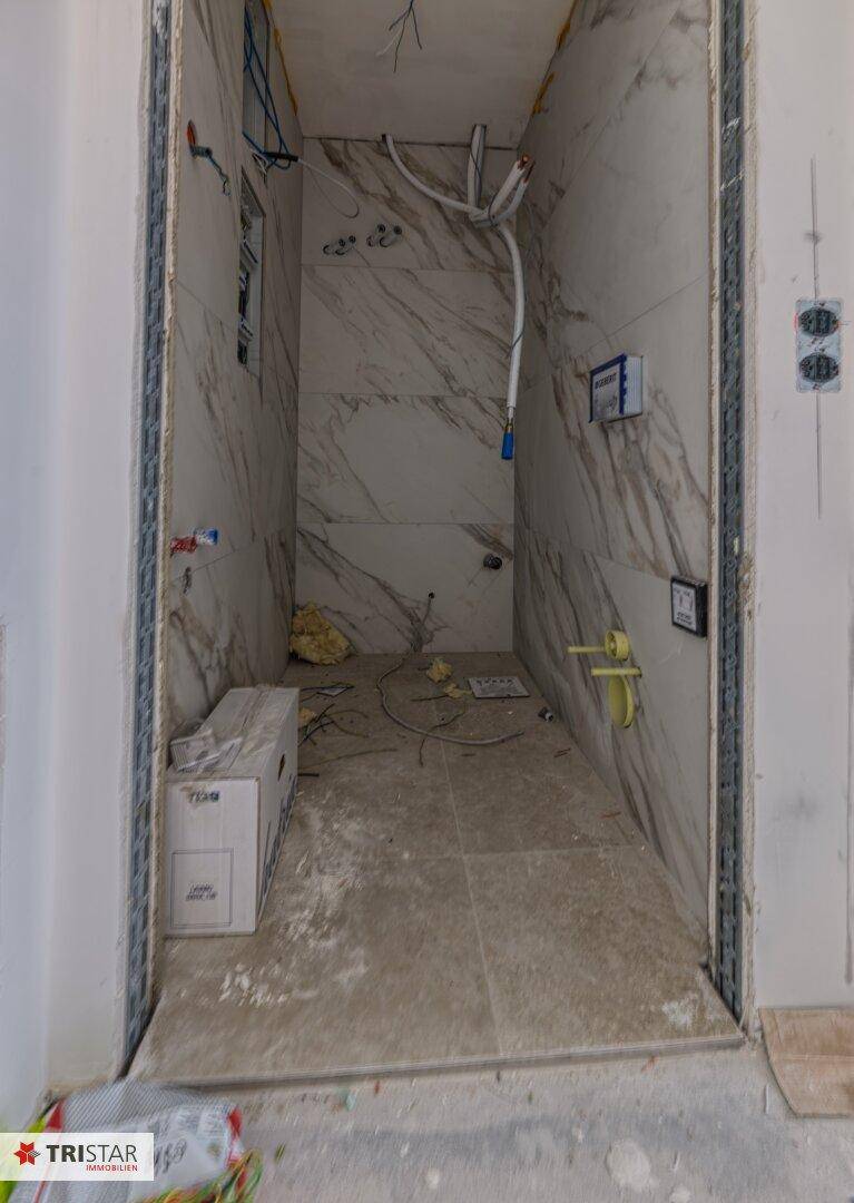Unfertiges Badezimmer mit Marmoroptik-Fliesen an den Wänden und sichtbaren Installationen.