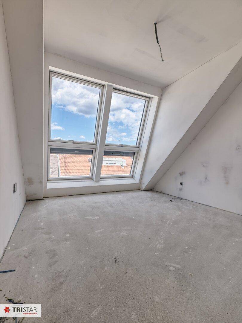 Helles Dachgeschosszimmer im Rohbau mit großen Dachfenstern und schrägen Wänden.