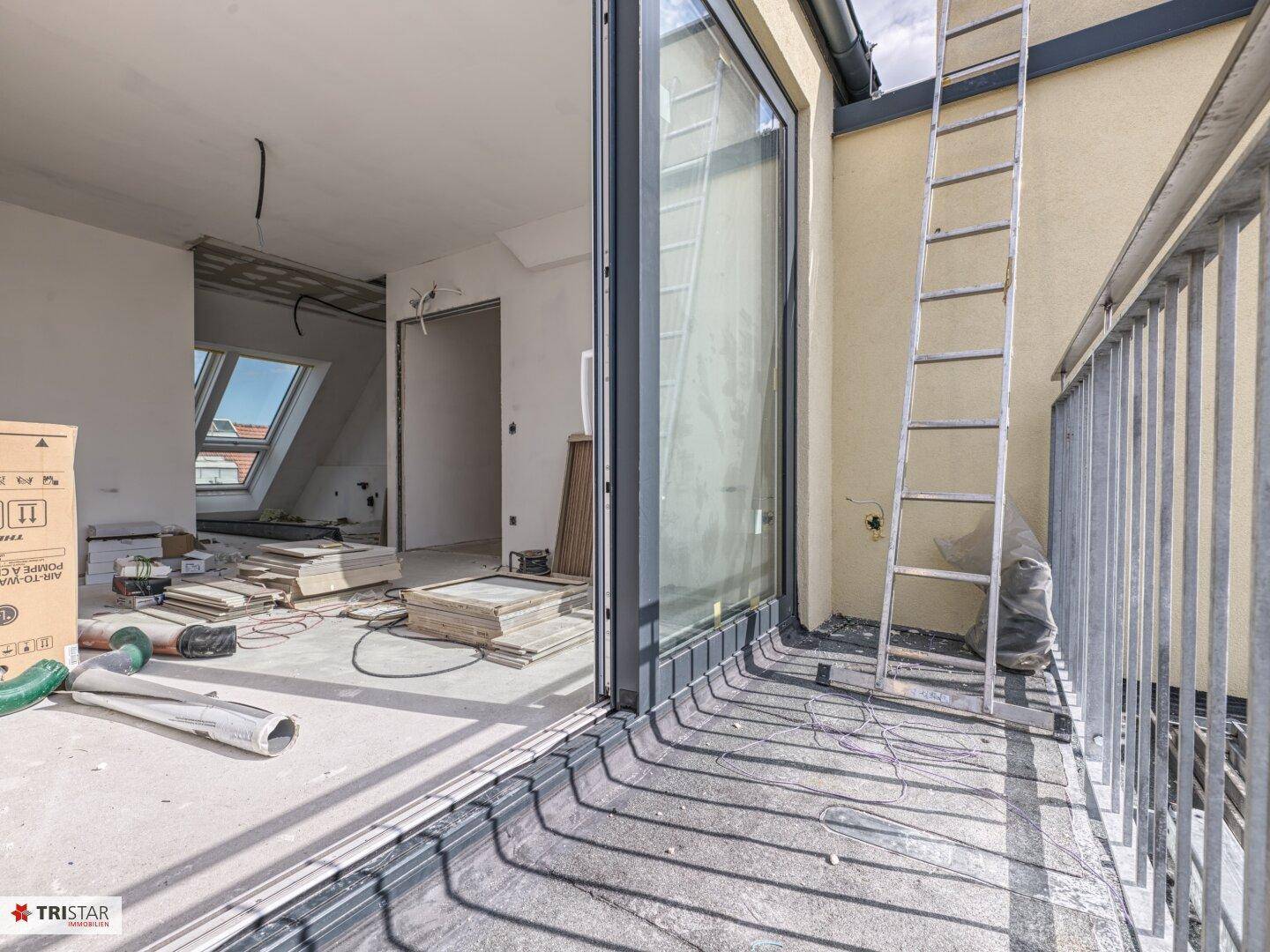 Unfertiger Innenraum mit Zugang zu einem Balkon und Blick auf weitere Dachgeschossräume.