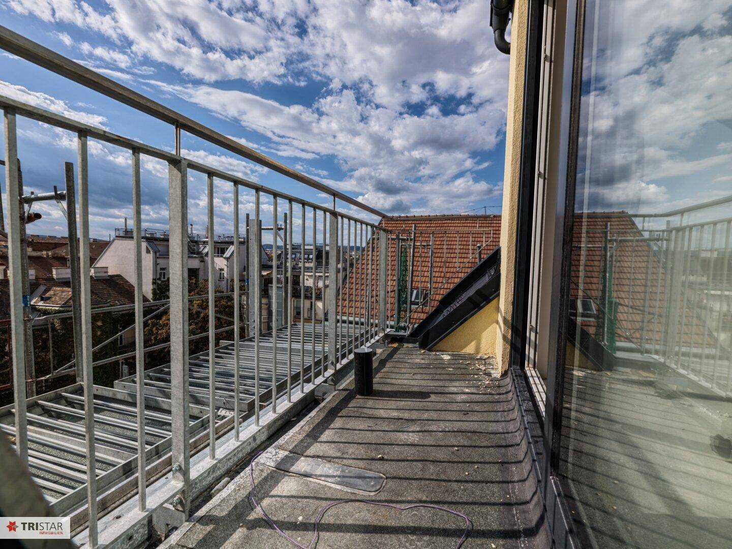 Balkon im Bau mit Metallgeländer und Blick über die Dächer der Stadt.