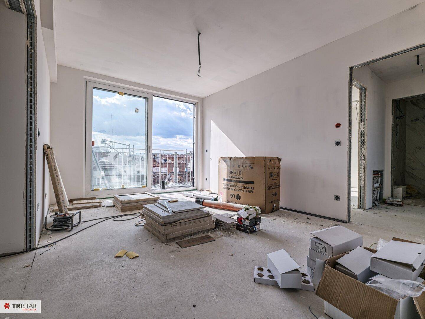 Unfertiger Innenraum mit großen Schiebetüren zum Balkon und Baumaterialien auf dem Boden.