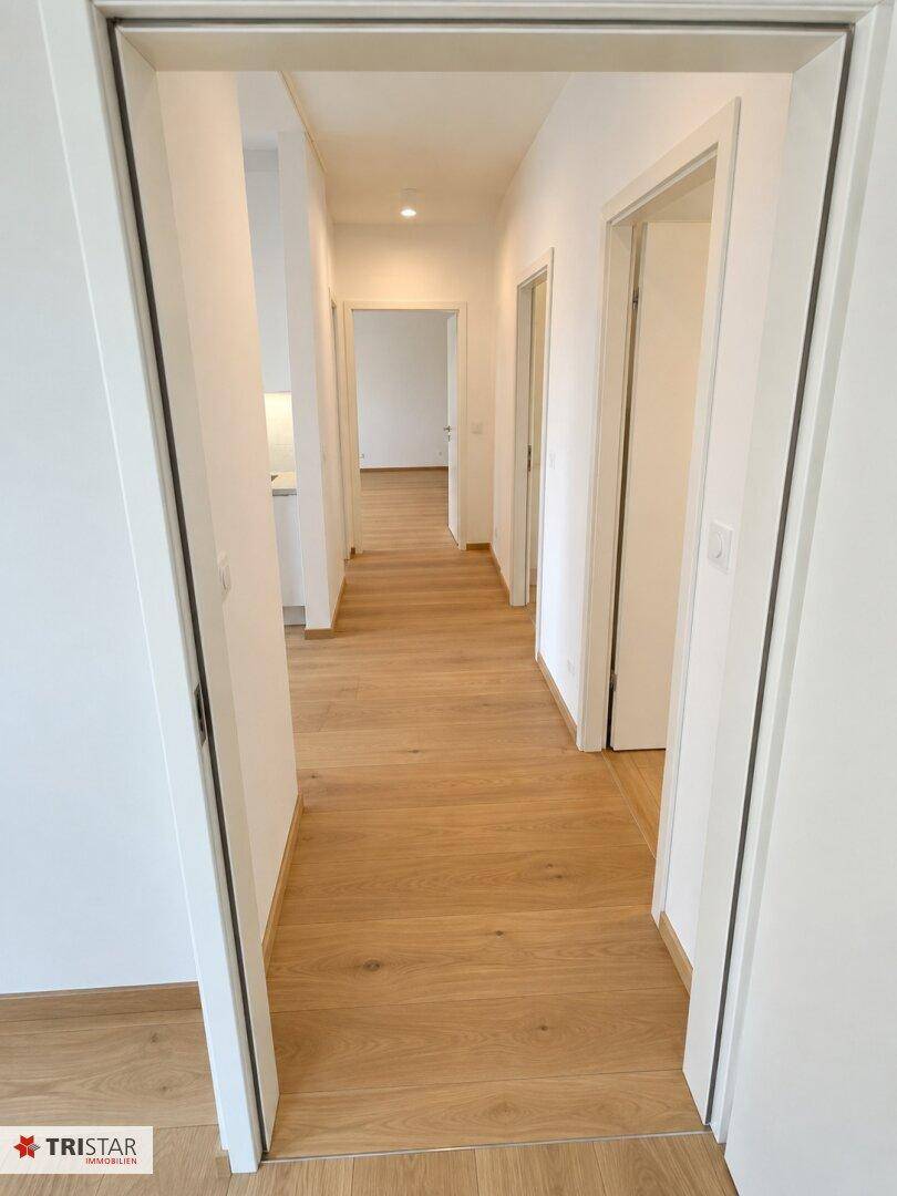 Langer, heller Flur mit Holzfußboden, der zu verschiedenen Räumen der Wohnung führt.