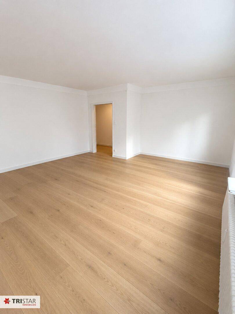 Geräumiges, helles Zimmer mit Parkettboden und Zugang zu einem weiteren Raum, ideal für Wohnzwecke.