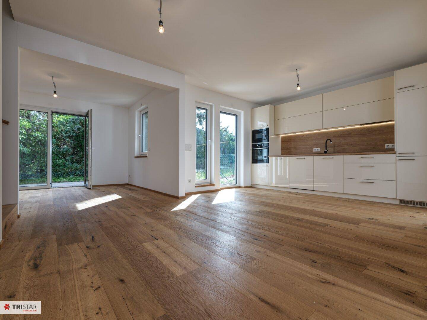 Heller offener Wohnbereich mit moderner Einbauküche, Holzboden und Zugang zum Garten.