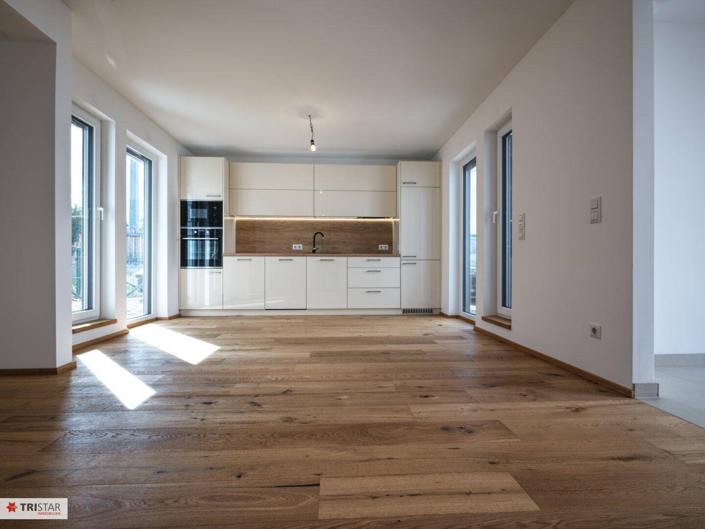 Moderne Küche mit weißen Schränken, Holzakzenten und großen Fenstern für viel Helligkeit.