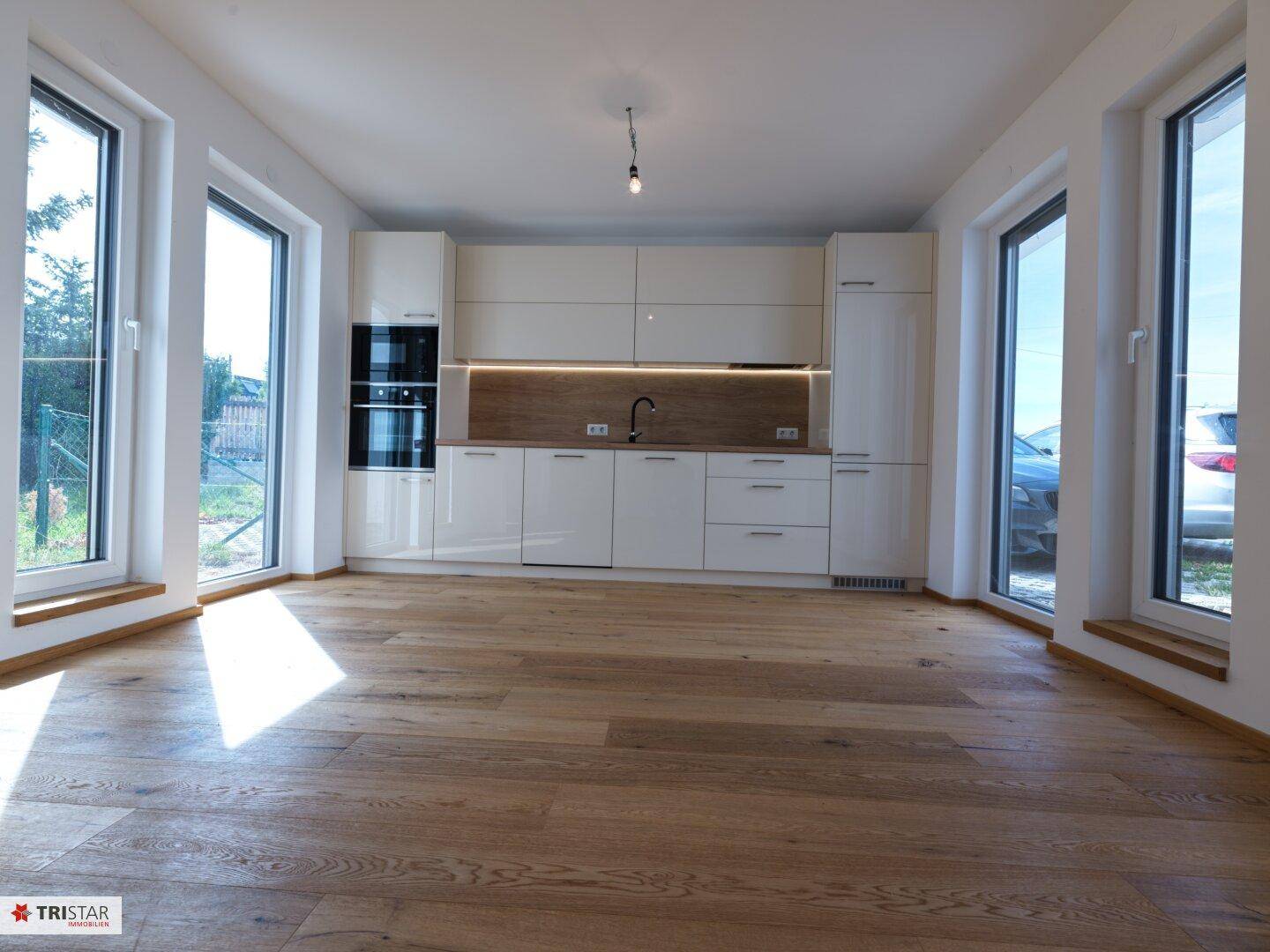 Moderne Einbauküche mit weißen Hochglanzfronten, Holzarbeitsplatte und viel Tageslicht.