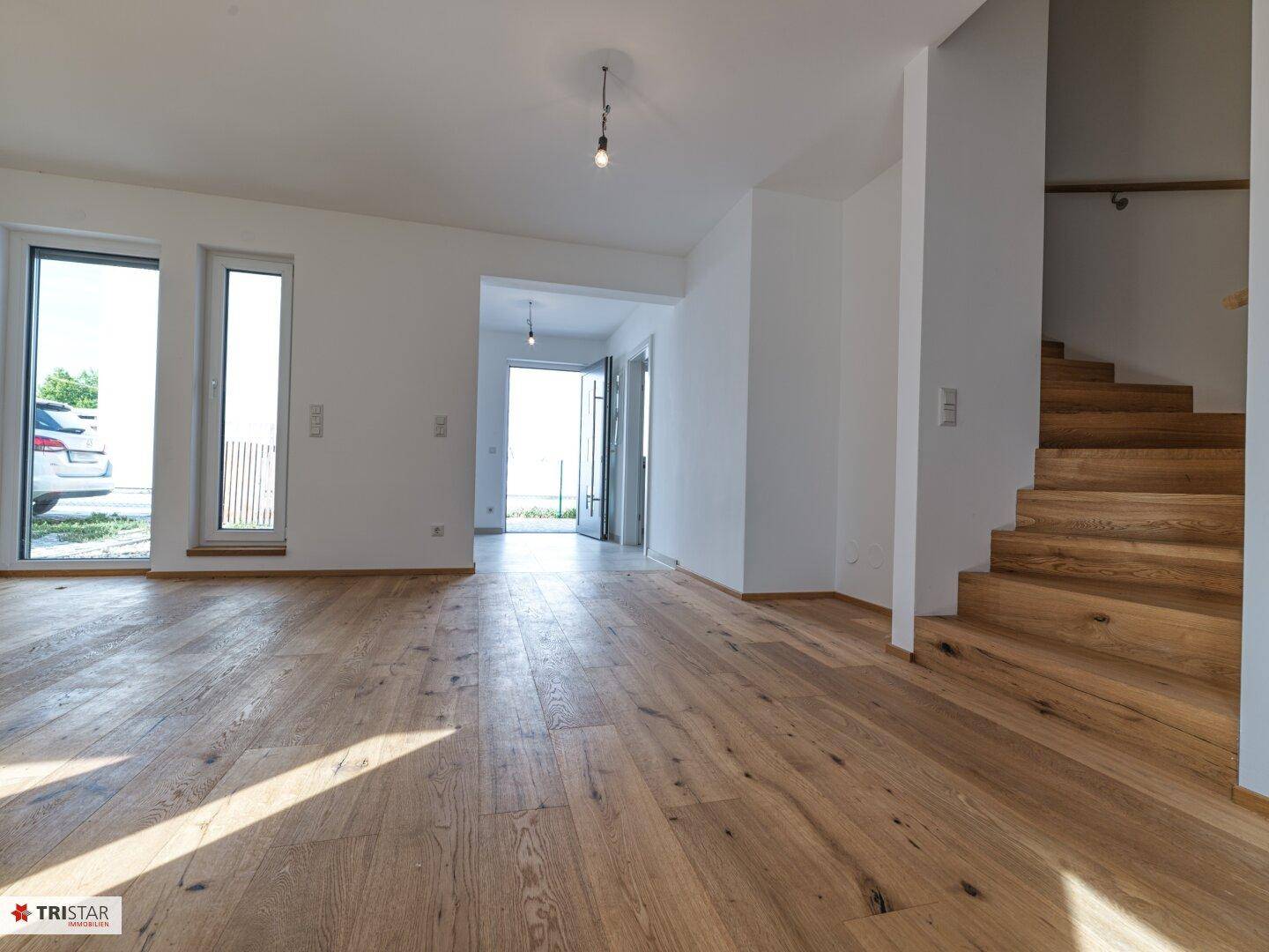 Heller Eingangsbereich mit Holzboden, Treppe und Blick in den offenen Wohnbereich.