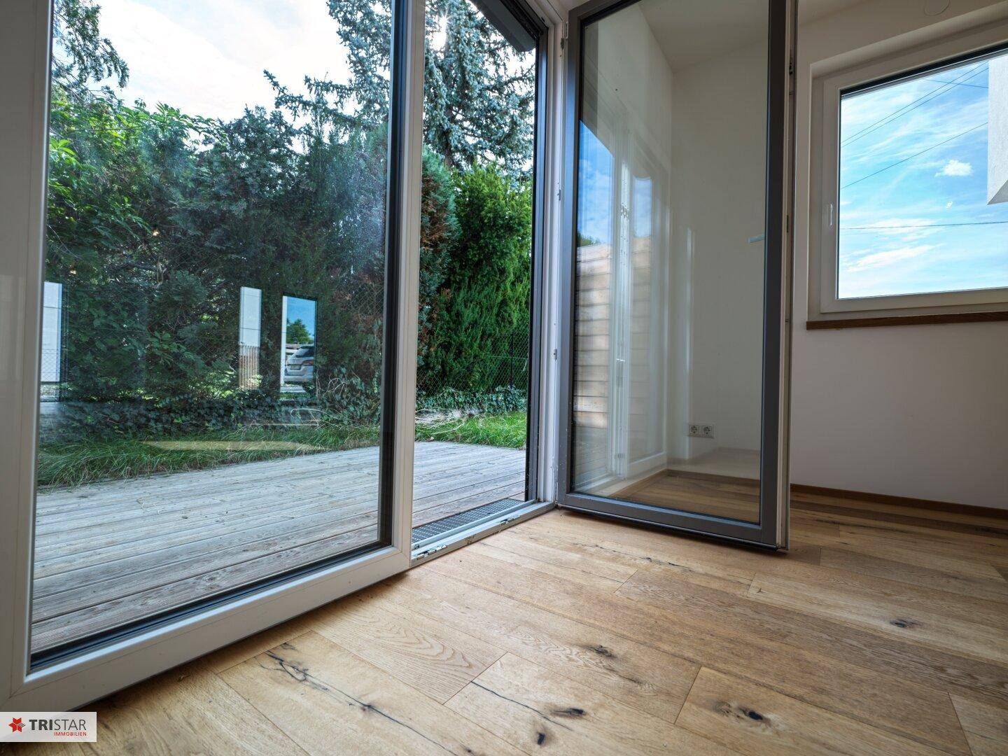 Heller Wohnraum mit Holzboden und großen Schiebetüren, die zur Holzterrasse und in den Garten führen.
