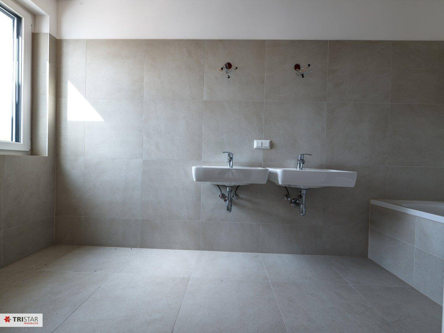 Modernes Badezimmer mit Doppelwaschbecken, Badewanne und hellen Fliesen, bereit zur Fertigstellung.