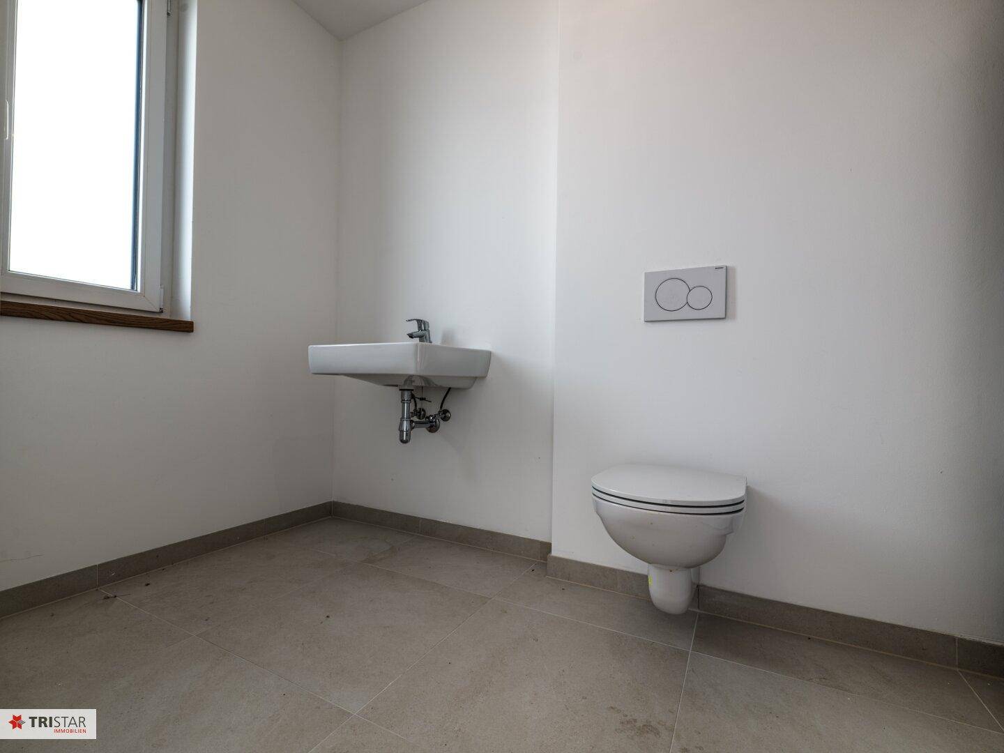 Helles Gäste-WC mit wandhängendem WC, kleinem Waschbecken und Fenster.