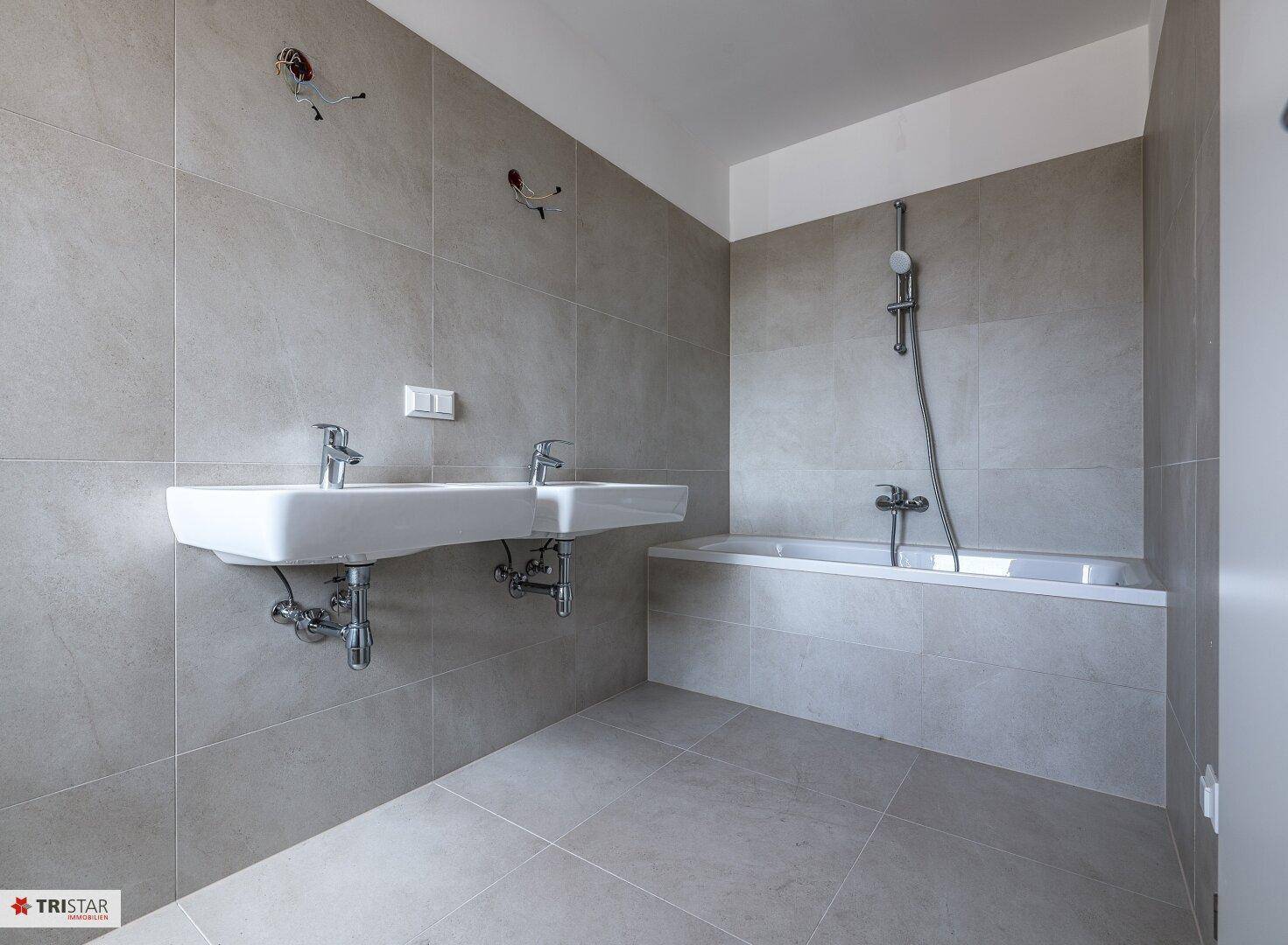 Helles Badezimmer mit Doppelwaschbecken, Badewanne und Duscharmatur, in modernem Design.