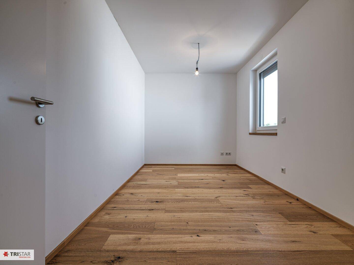 Helles, leeres Zimmer mit neuem Holzboden und einem Fenster, ideal als Schlafzimmer.