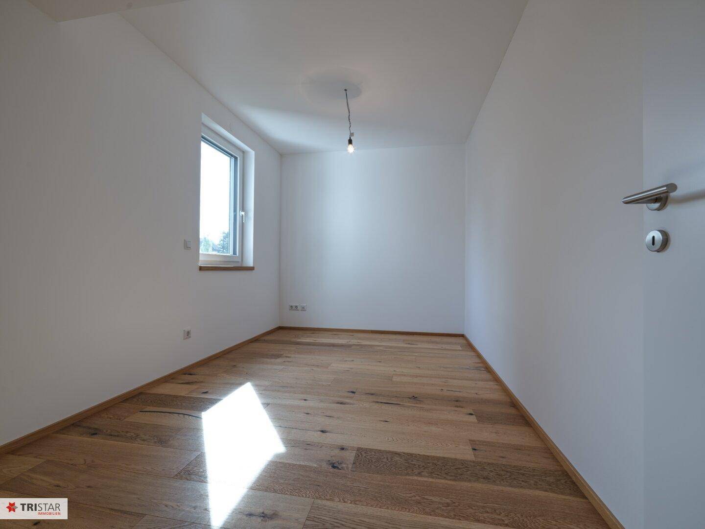 Lichtdurchflutetes Zimmer mit Eichenparkett und weiß gestrichenen Wänden, sehr hell.