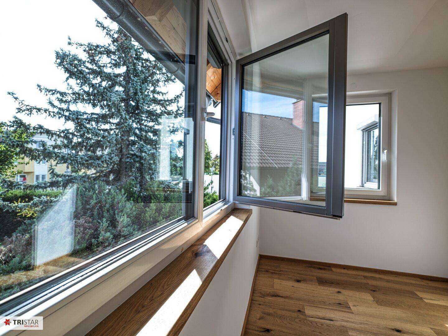 Detailansicht eines geöffneten Fensters mit Blick ins Grüne und auf die Umgebung.