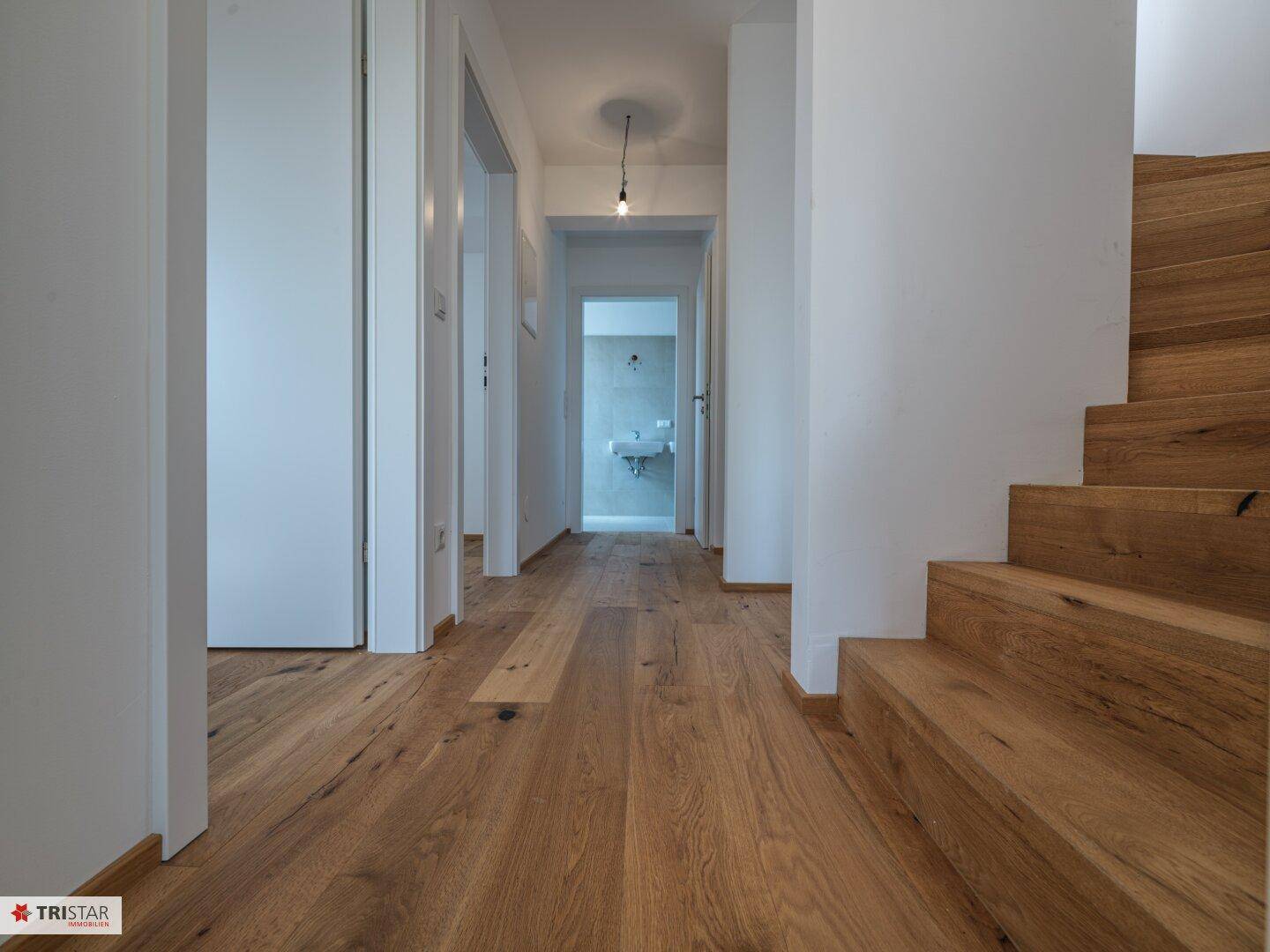 Langer Flur mit Holzboden und Zugang zu weiteren Räumen, inklusive Badezimmer am Ende.