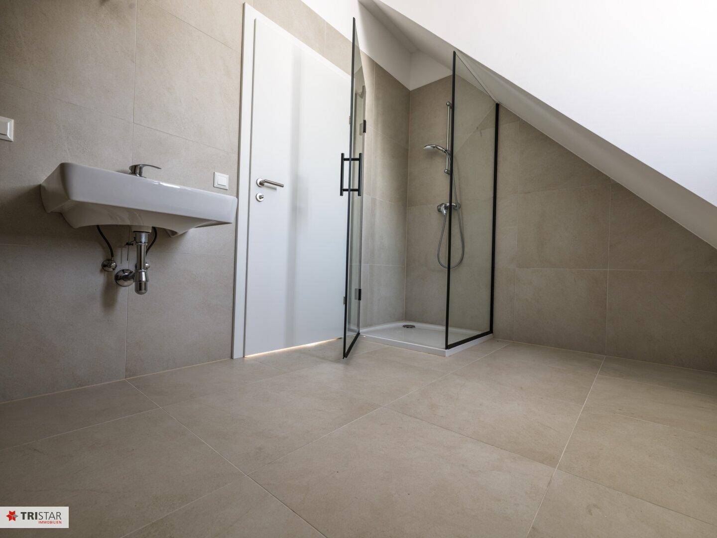 Modernes Badezimmer im Dachgeschoss mit Dusche, Waschbecken und schrägen Wänden.