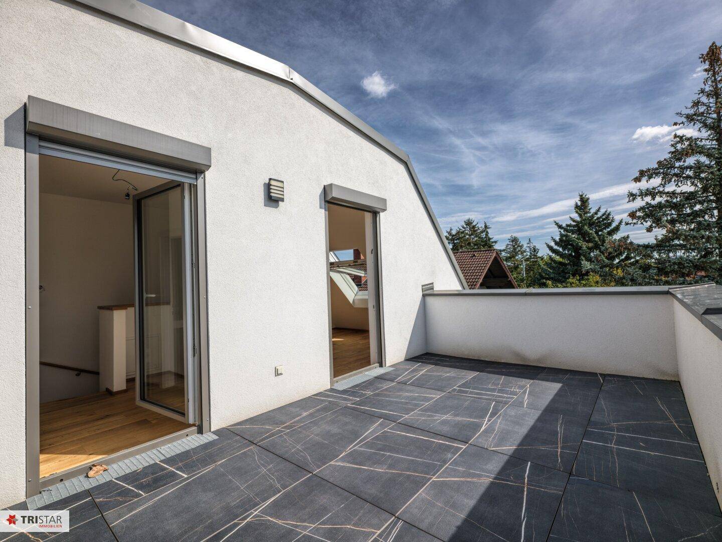 Große Dachterrasse mit dunklen Fliesen und Zugang zu den Innenräumen, umgeben von Grün.