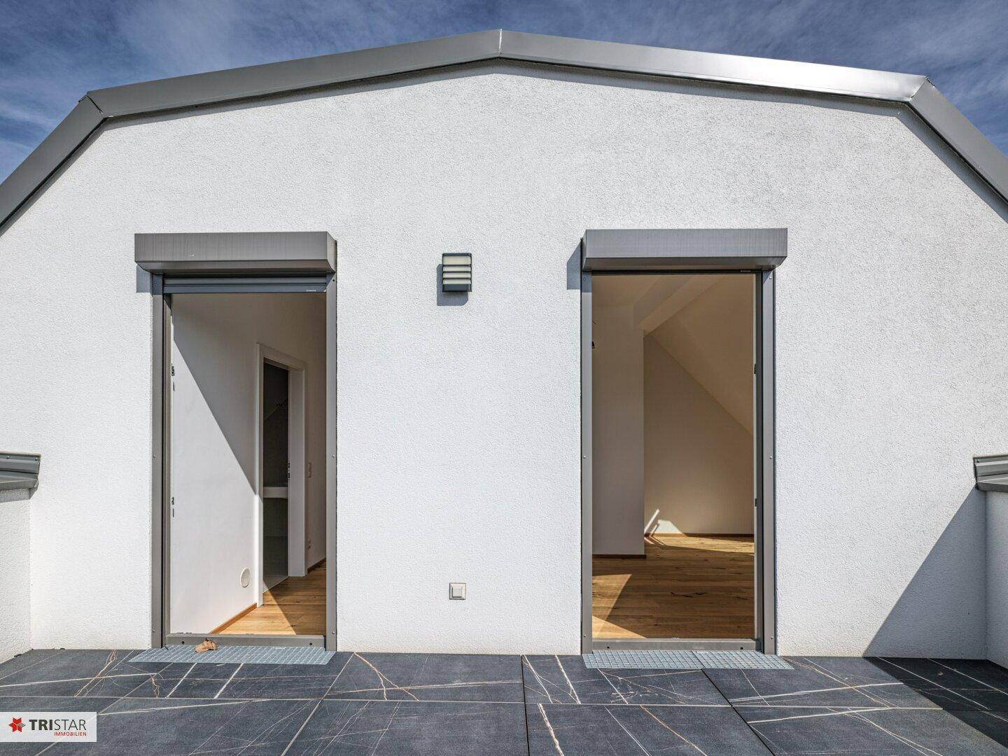 Moderne Fassade mit zwei großen Glastüren, die auf eine geräumige Dachterrasse führen.