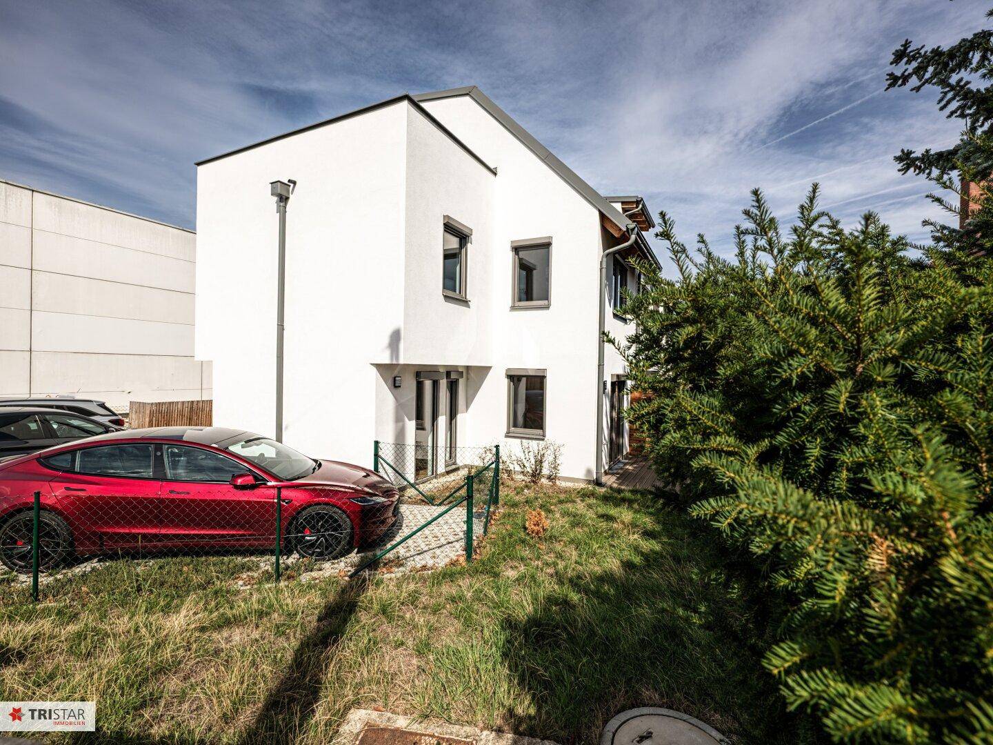 Vorderansicht eines modernen Einfamilienhauses mit weißer Fassade und einem roten Auto auf dem Stellplatz.