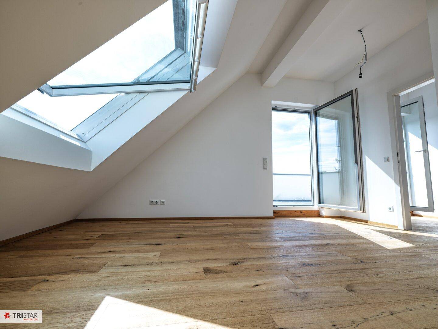 Helles Zimmer im Dachgeschoss mit Holzboden, Dachfenster und Zugang zur Terrasse.