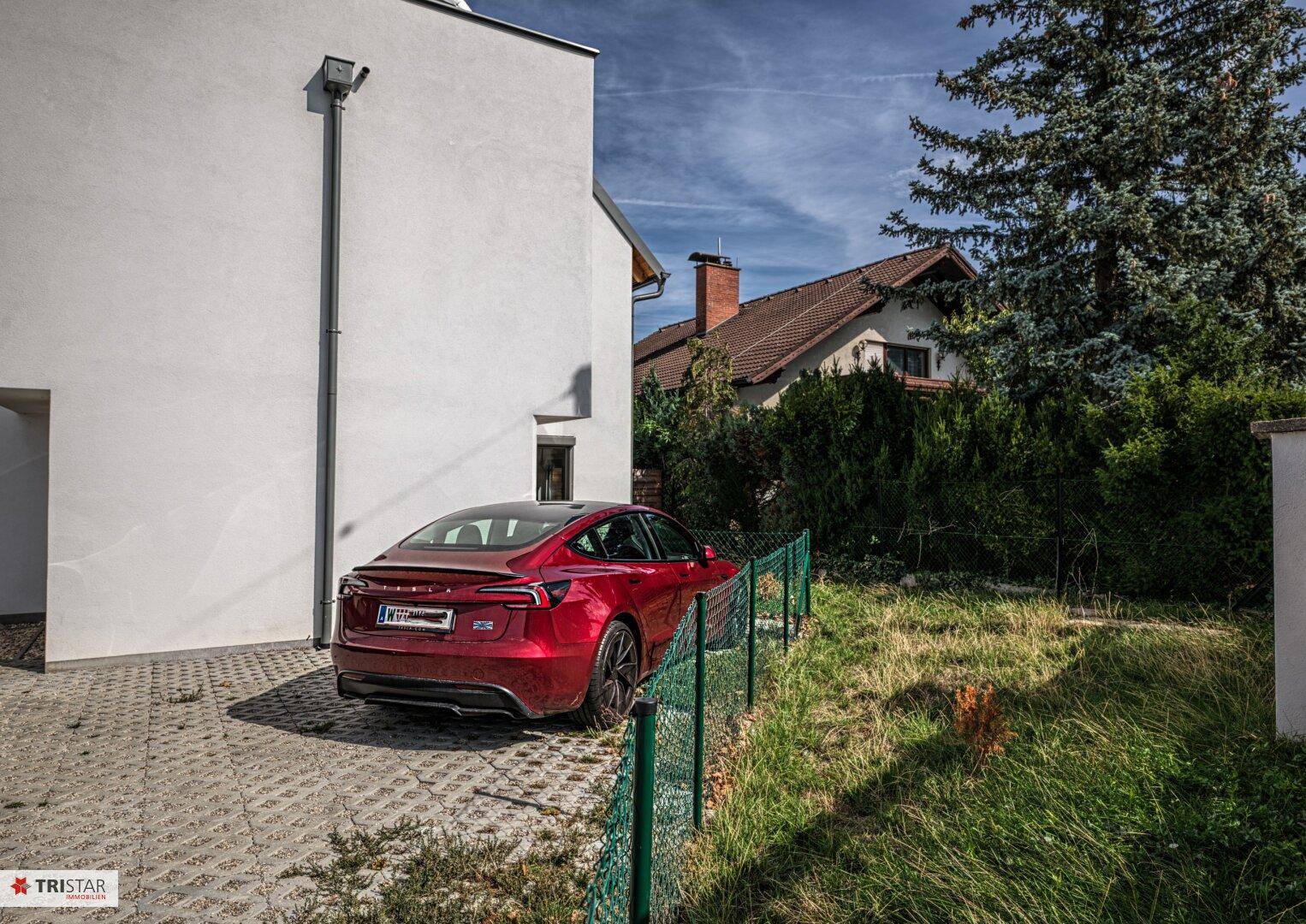 Seitenansicht eines modernen Hauses mit gepflasterter Auffahrt und einem roten Elektroauto.