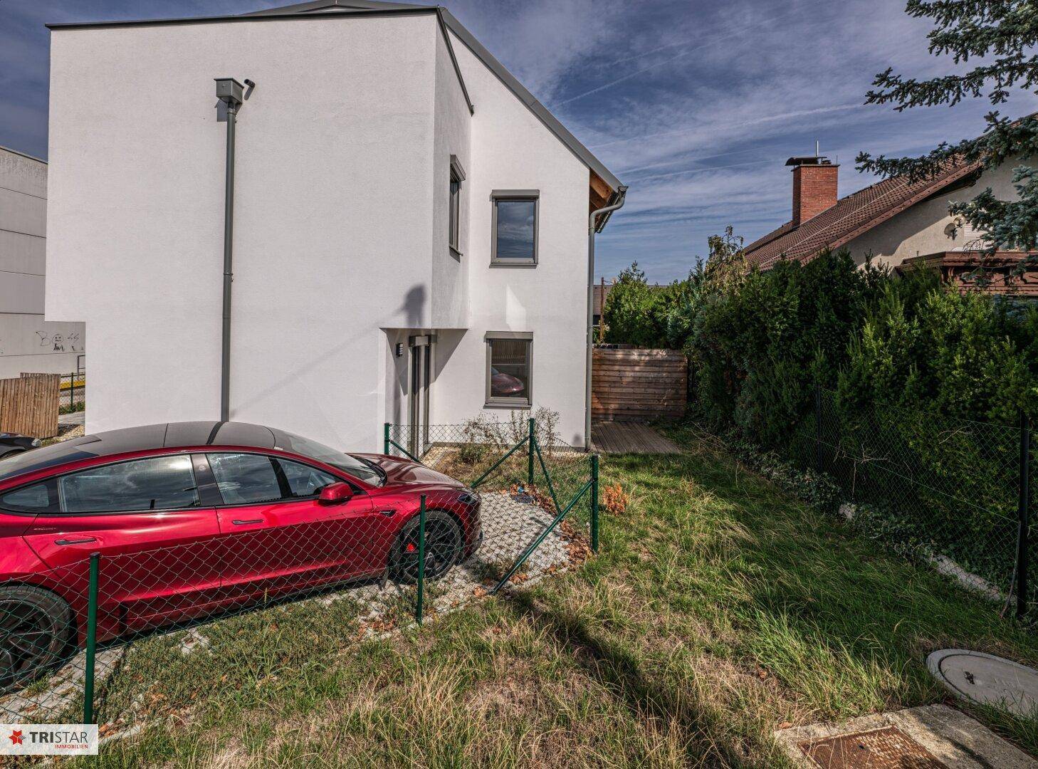 Seitenansicht des modernen Hauses mit einem roten Auto auf dem Rasenparkplatz.