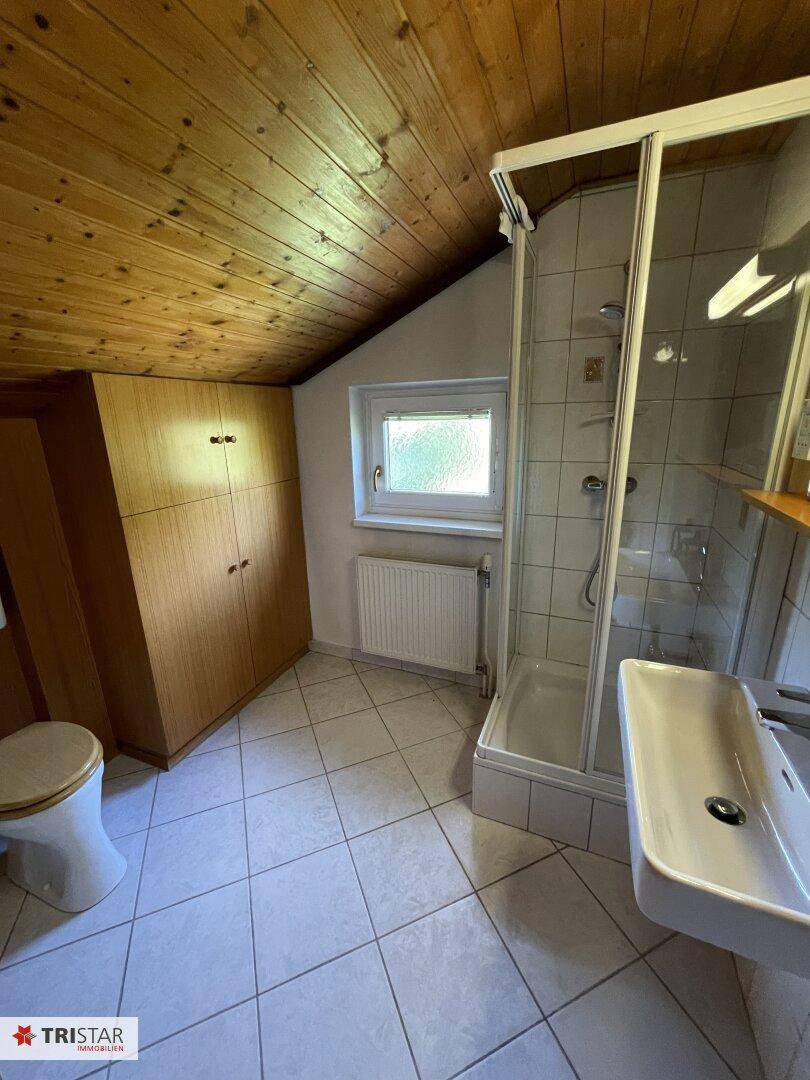 Dachgeschoss-Badezimmer mit Duschkabine, Waschbecken, WC und Holzdecke.