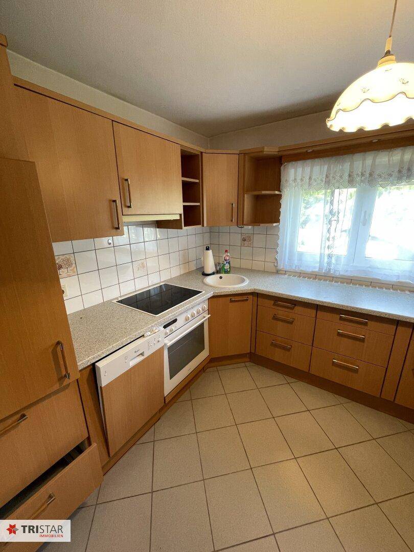 Traditionelle Küche mit Holzschränken, Einbaugeräten und Fenster mit Vorhang.