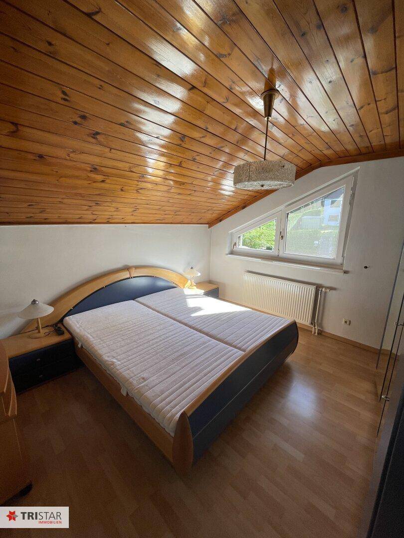 Schlafzimmer mit Doppelbett, Holzdecke und Laminatboden im Dachgeschoss.
