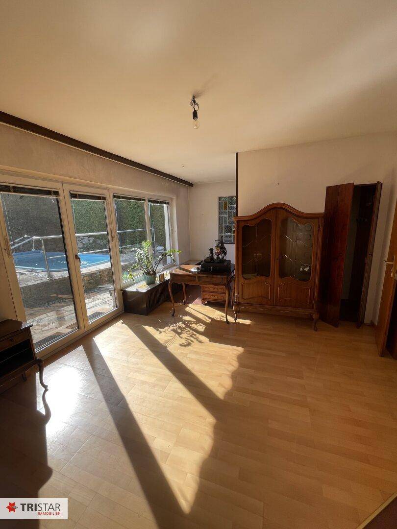 Geräumiges Wohnzimmer mit Holzboden, großen Fenstern und Zugang zum Außenbereich.