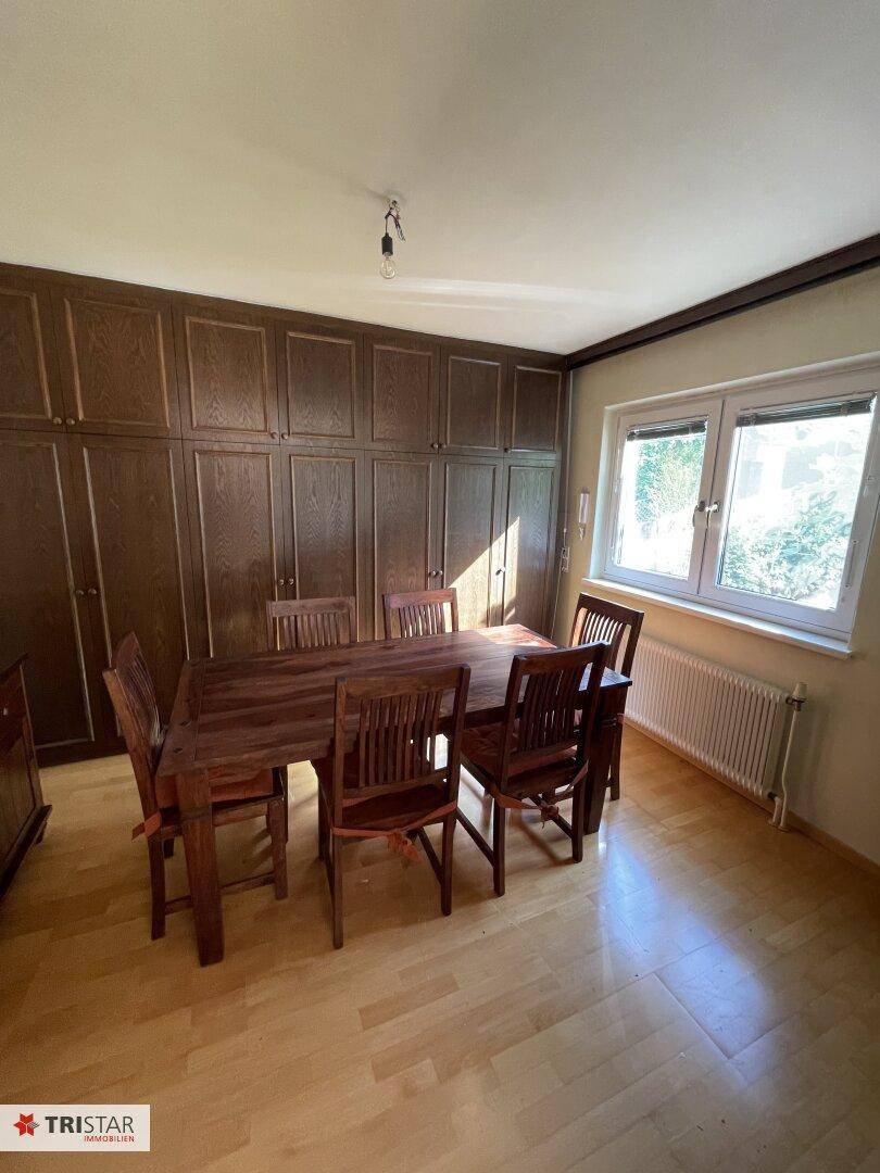 Esszimmer mit großem Holztisch, Stühlen und Einbauschränken entlang der Wand.