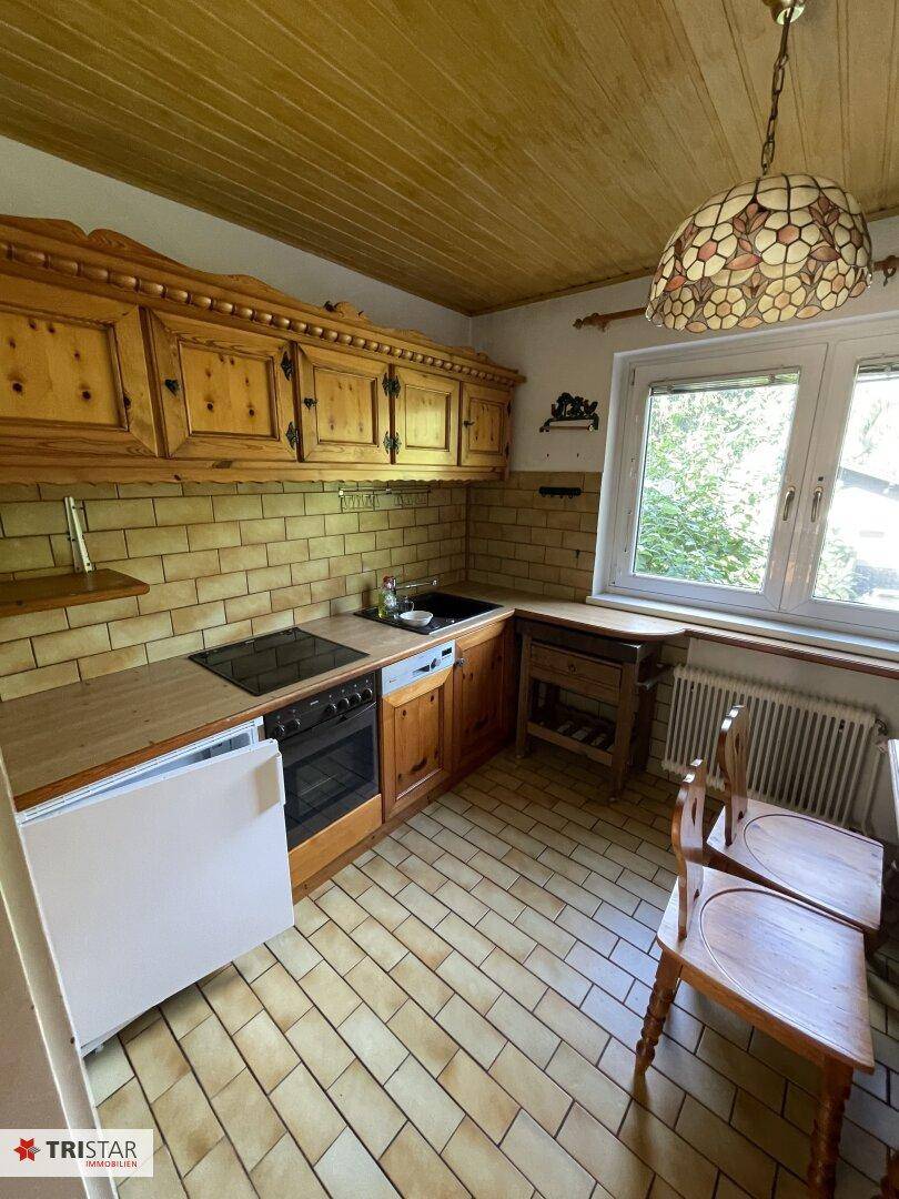 Rustikale Küche mit Holzschränken, Fliesenboden und Fenster mit Blick ins Grüne.