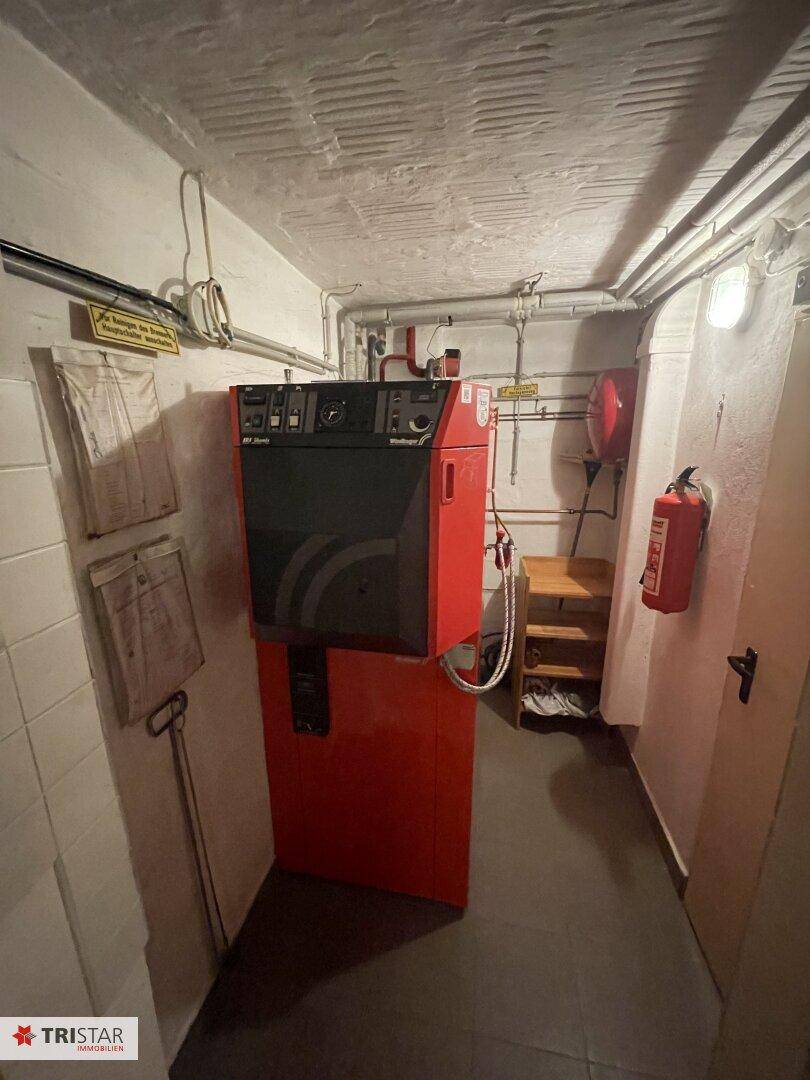 Heizungsraum im Keller mit großem roten Heizkessel und sichtbaren Rohrleitungen.