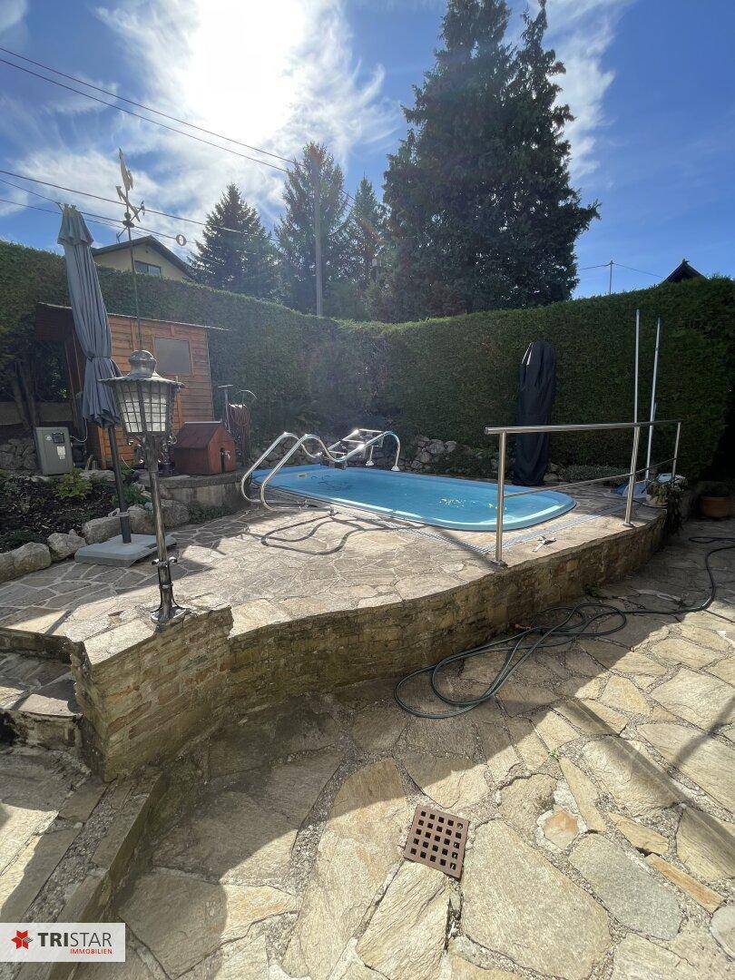 Sonniger Gartenbereich mit eingelassenem Pool und rustikaler Steinterrasse, ideal für Entspannung im Freien.