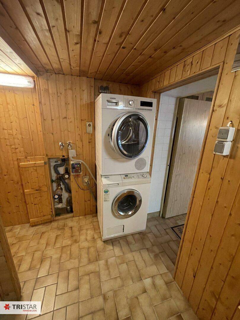 Hauswirtschaftsraum mit Waschmaschine und Trockner, Holzwänden und praktischem Fliesenboden.
