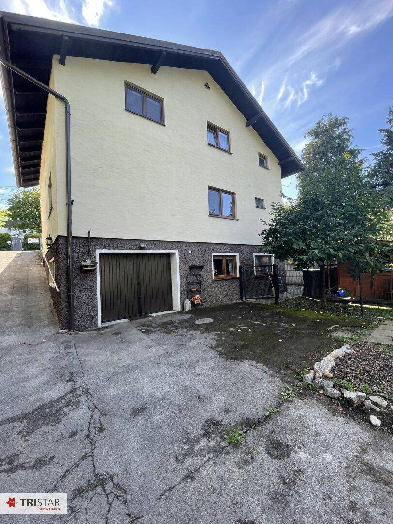 Seitenansicht des Hauses mit Garage im Untergeschoss und gepflasterter Zufahrt.