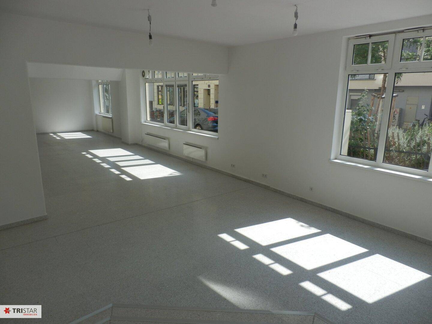 Geräumiger, heller Gewerberaum mit großen Fenstern, die viel natürliches Licht hereinlassen und eine offene Atmosphäre schaffen.