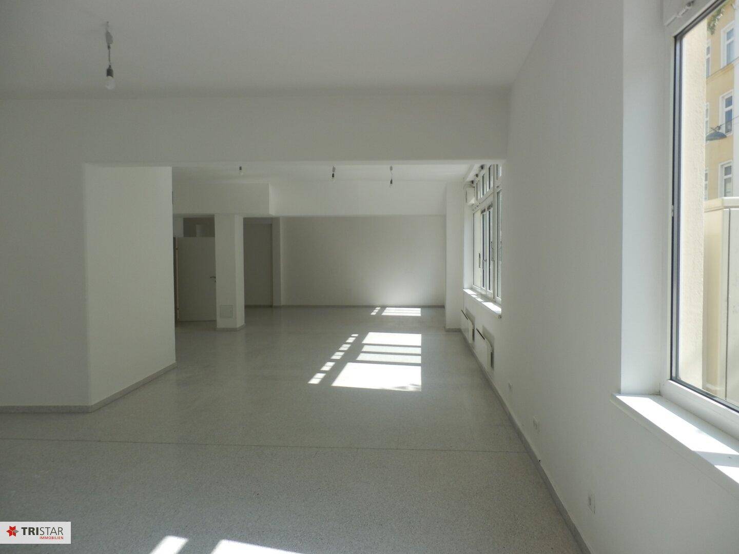 Weiter Blick in einen leeren, hellen Gewerberaum mit großen Fenstern und sauberem Boden, ideal für verschiedene Nutzungen.