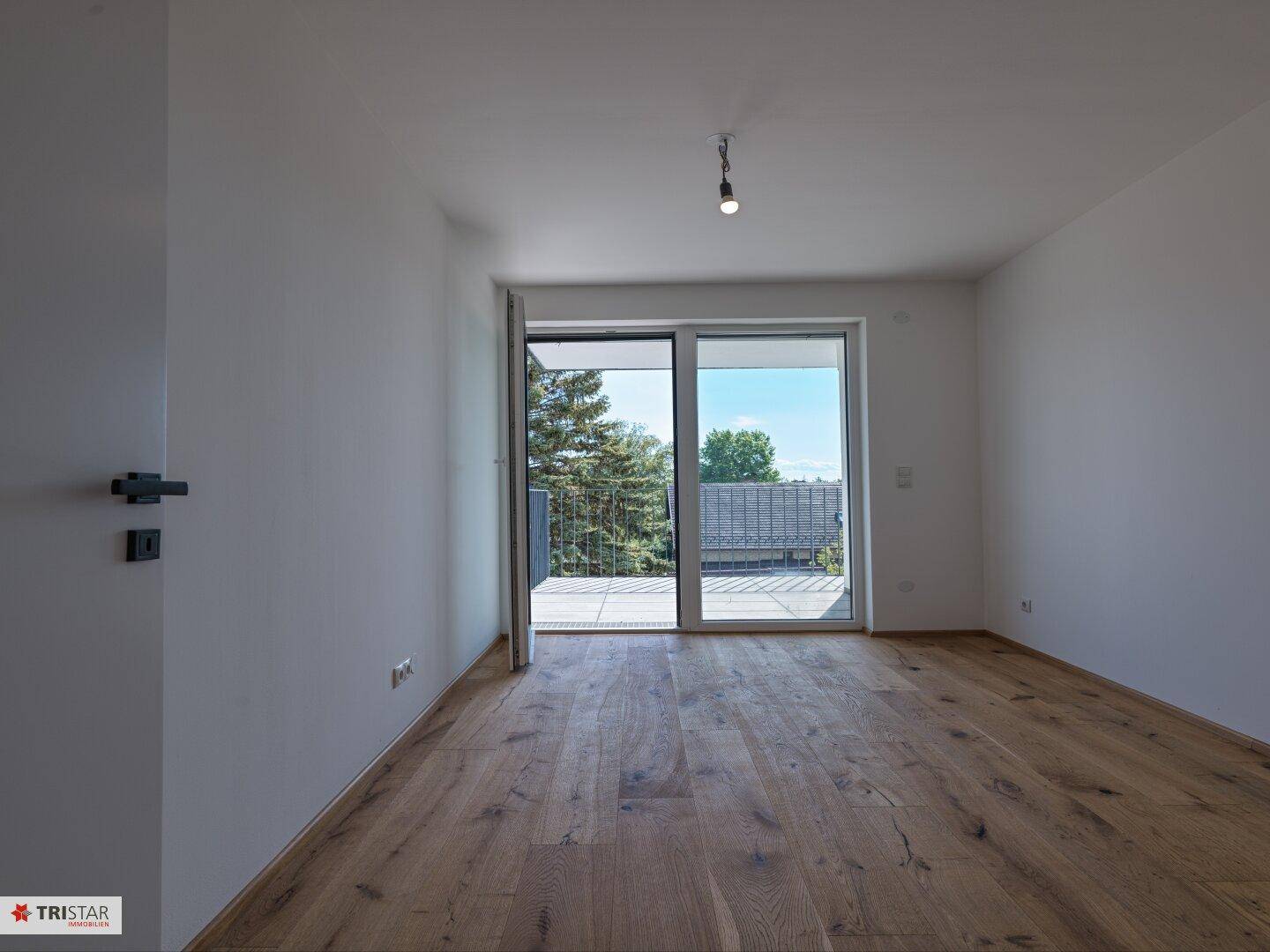 Geräumiges Zimmer mit Holzboden und Balkonzugang, bietet viel natürliches Licht.