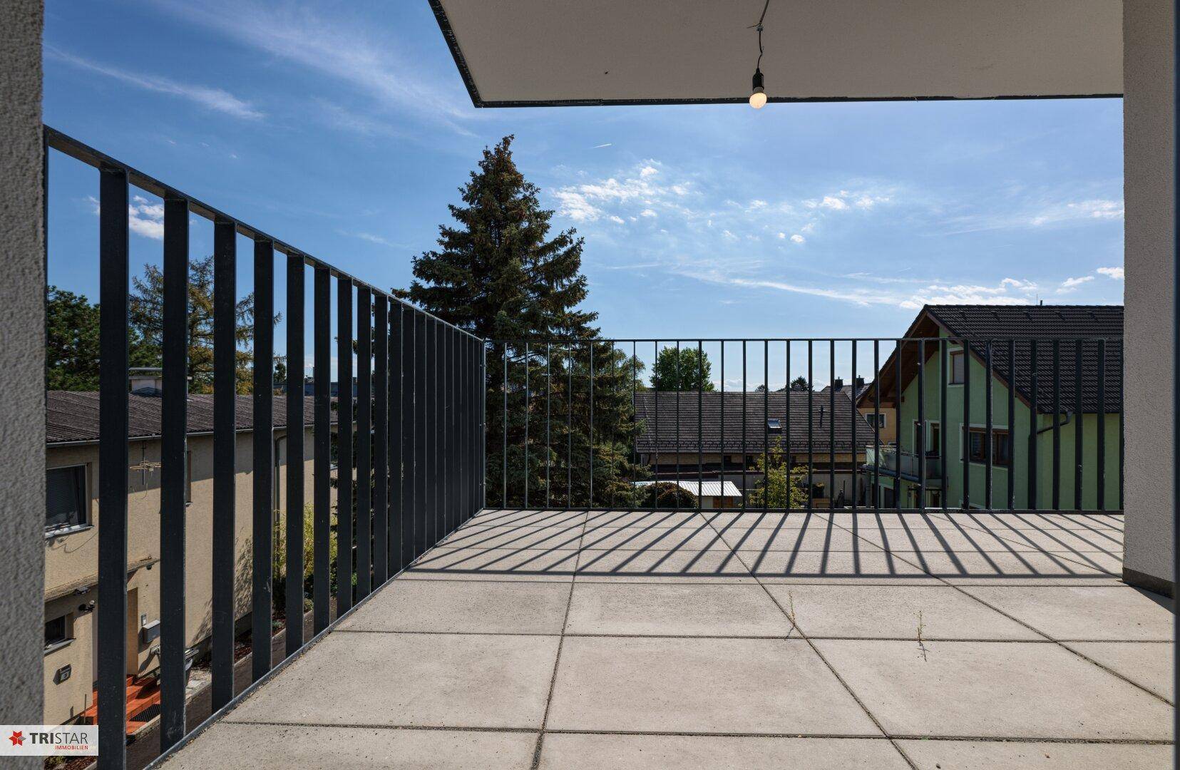Geräumiger Balkon mit Fliesenboden und Metallgeländer, bietet einen Blick ins Grüne.