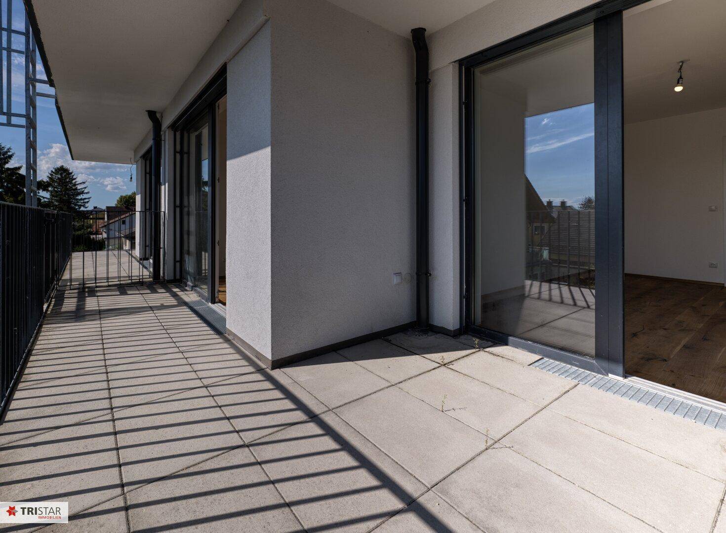 Langer Balkon mit Fliesenboden und Zugang zu mehreren Räumen, ideal für Entspannung.