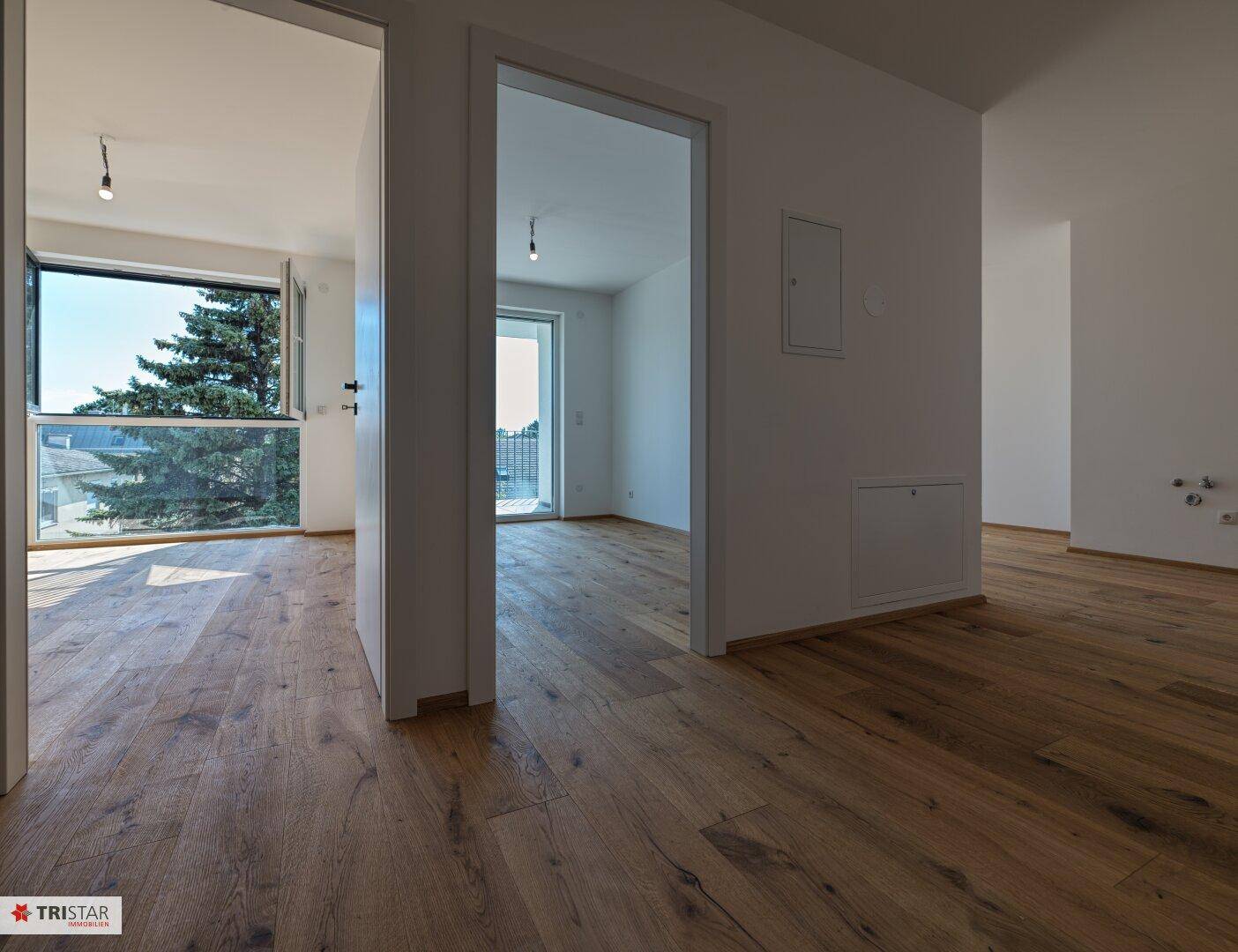 Heller Flur mit Holzboden, der zu verschiedenen Zimmern und einem Balkon führt.