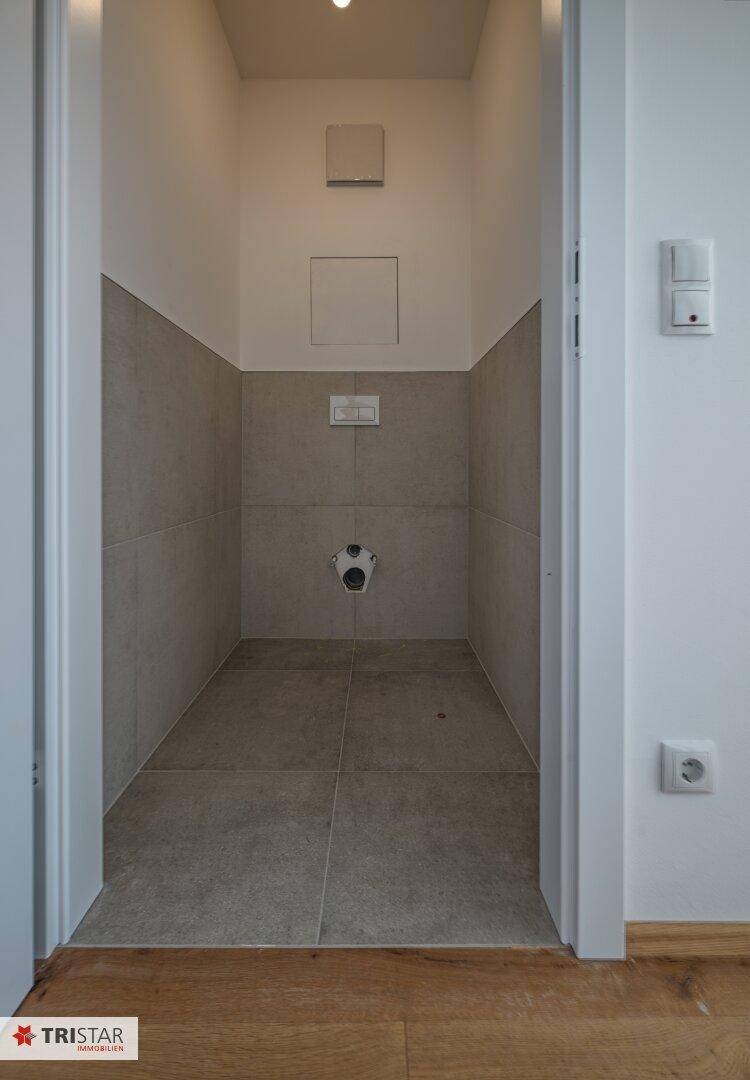 Separates WC mit grauen Fliesen und Vorbereitung für eine Wandtoilette.