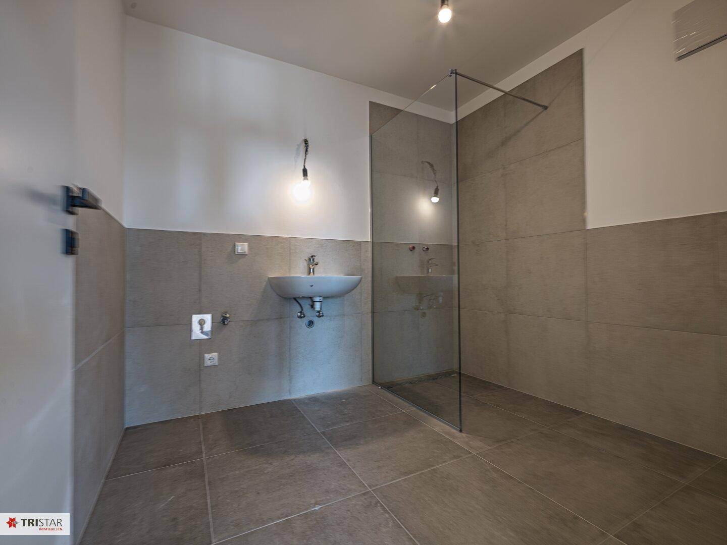 Modernes Badezimmer mit begehbarer Dusche, Waschbecken und grauen Fliesen.