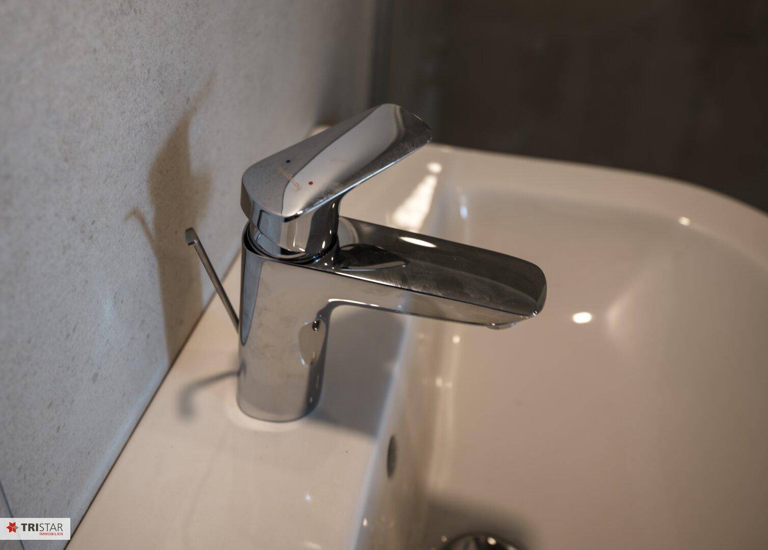 Moderner Wasserhahn über einem Waschbecken in einem Badezimmer mit schlichtem Design.