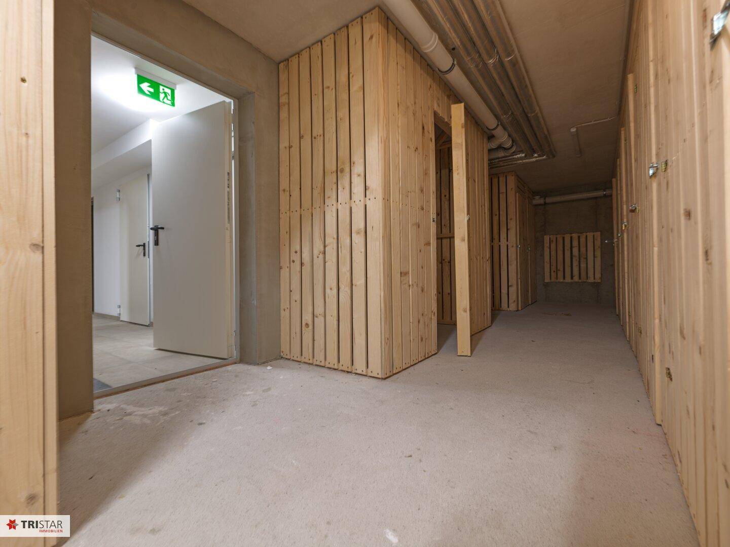 Kellerraum mit Holzverschlägen für zusätzlichen Stauraum und Betonboden.