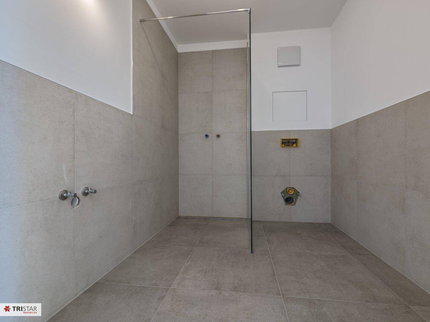 Modernes Badezimmer im Bau mit grauen Fliesen und vorbereiteter Duschkabine.