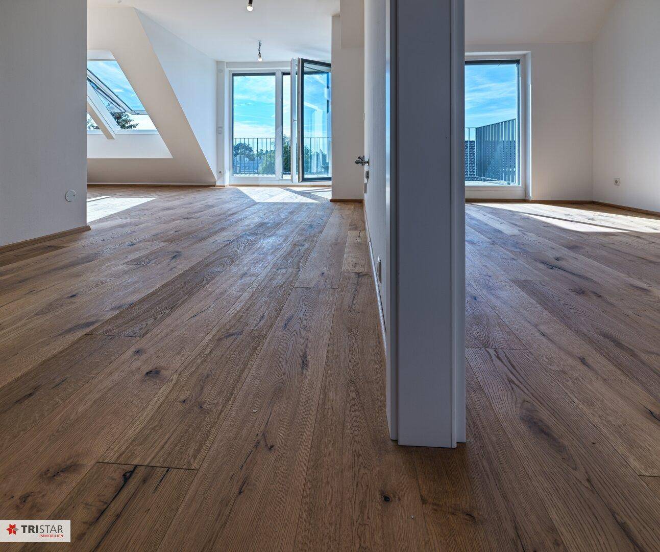 Heller Innenraum mit Holzboden und großen Fenstern, die viel Licht hereinlassen.