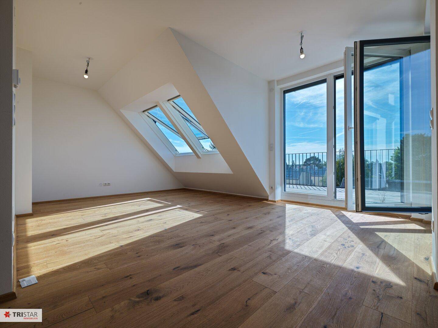 Heller Raum mit Holzboden, großen Fenstern und Zugang zur Dachterrasse.